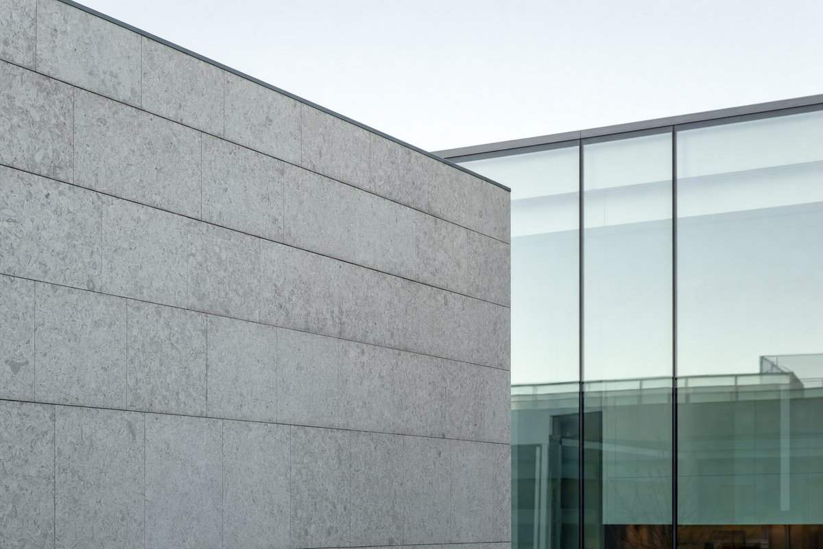 Eine graue Steinmauer trifft auf eine schlichte Glasfassade im Winterlicht