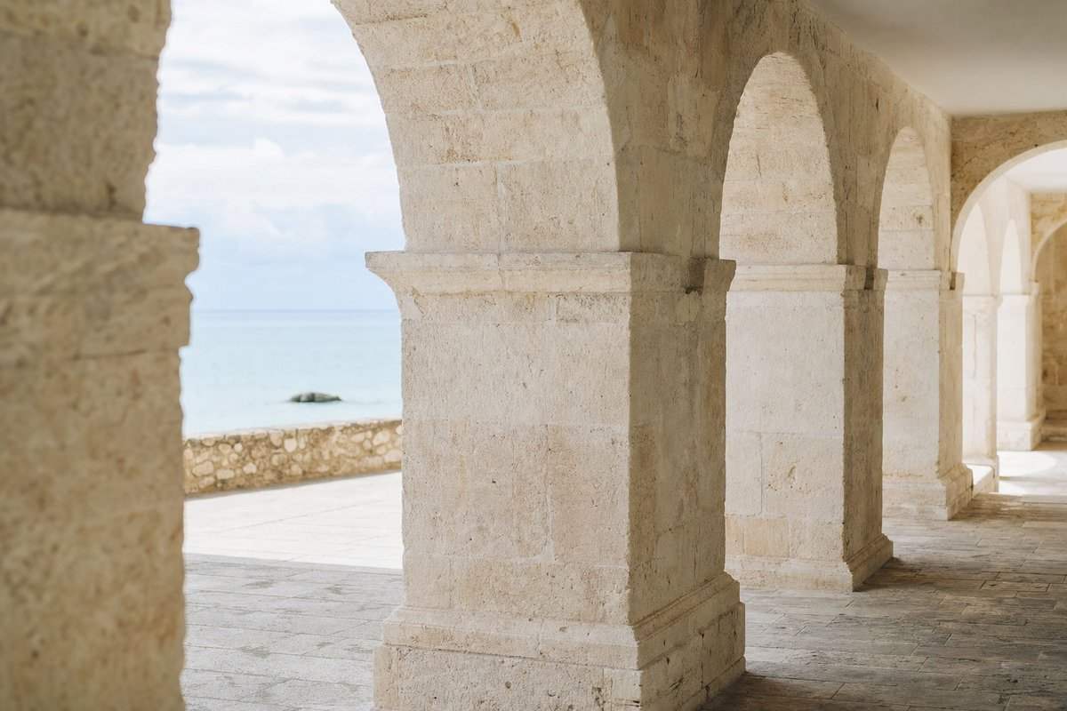 Eine helle Kalksteinarkade mit tiefen Bogenschatten und Meer im Hintergrund